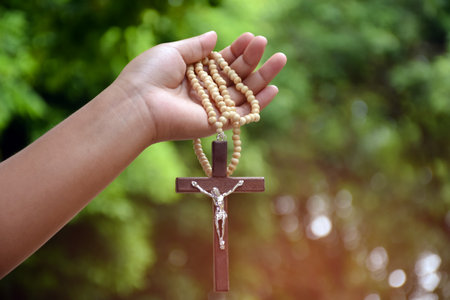 Wooden cross bead necklace holding in hands, natural blurr bokeh background, soft and selective focus.の写真素材