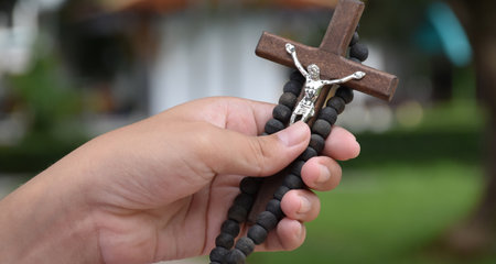 Wooden cross and wooden rosary are held in hands of young asian Catholic prayer while praying in the temple park area.の写真素材