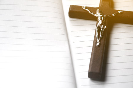 Closeup wooden cross which has a metal statue of crucified Jesus on notebook, concept for praying in a local church, soft and selective focus.の写真素材