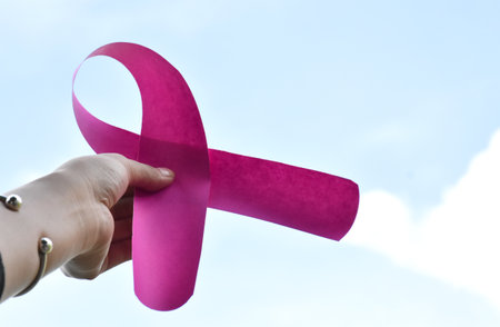 Pink paper ribbon holding in hands of female teenager to show and to call out all people around the world to support and to attend the breast cancer campaign of woman.の写真素材