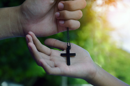 Asian young Christian boy shows his wooden rosary necklace with a cross, soft and selective focus,...