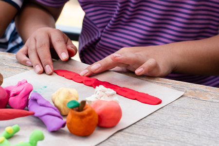 Children's hands are playing with plasticine on a wooden table.の写真素材