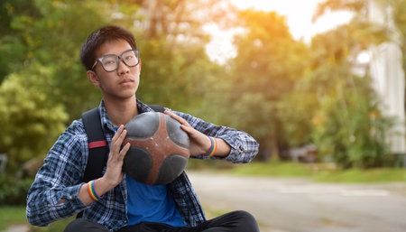 Young asian man sitting on the ground and holding a basketball ball.