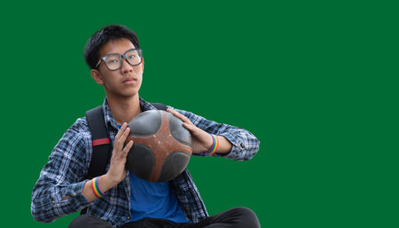 Young Asian college student holding a soccer ball on green screen background.の写真素材