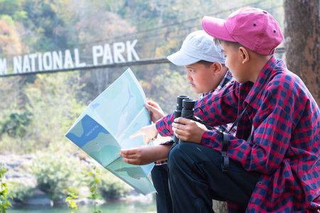 Asian boy sitting on the bridge and looking at the map in the forest