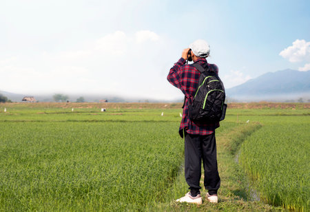 Asian man traveler with backpack and binoculars in the rice field.の写真素材