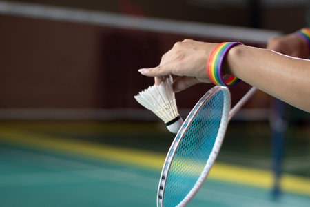 Badminton player wears rainbow wristbands and holding racket and white shuttlecock in front of the net before serving it to player in another side of the court, LGBT concept.の写真素材