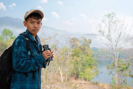 Young Asian man with backpack and binoculars looking at the lakeの写真素材