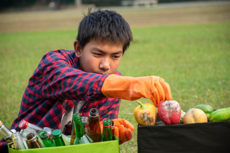 Asian boy in plaid shirt is separating garbages by himself at the park, soft and selective focus, environment care, community service and eco friendly concept.の写真素材
