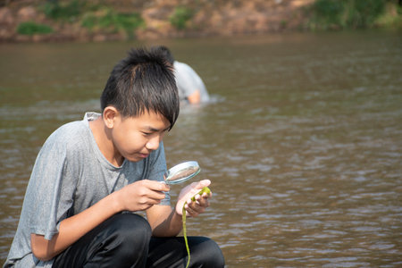 Asian boy holding magnifying glass on the river and looking at the freshwater algaeの写真素材