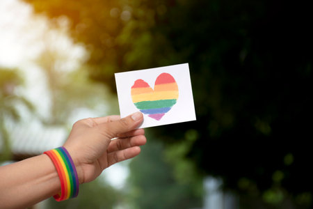 Woman hand holding a greeting card with LGBT rainbow heart on nature backgroundの写真素材