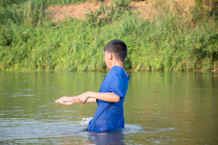 Asian boy in blue t-shirt is spending his freetimes by diving, swimming, throwing rocks and catching...