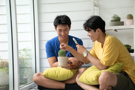 Young asian gay couple spending their free time, learning and looking after cactus pots on shelves behind by using magnifying glass, LGBT lover.の写真素材