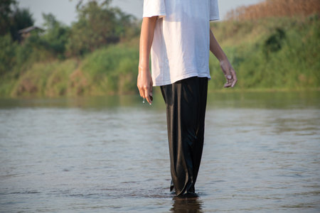 Asian boy is throwing rock over the surface of local river during his free time after school, in...