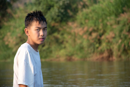 Asian boy is throwing rock over the surface of local river during his free time after school, in motion, concept for children hobby and childhood around the world.の写真素材