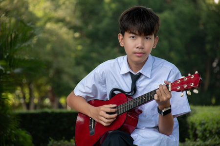 Asian boy playing guitar in the park. Education and music concept.