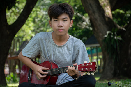 Asian young man playing guitar in the park, selective focus and shallow DOF.