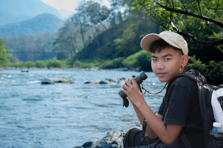 Young asian boy with binoculars sitting on the river bankの写真素材
