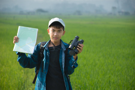 Young asian boy with backpack and binoculars in rice fieldの写真素材