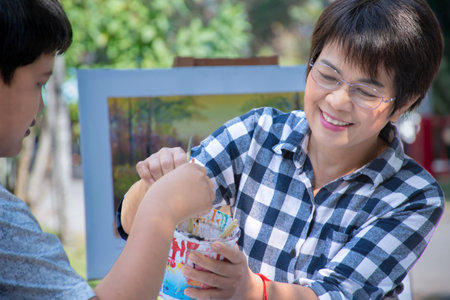 Asian kid painting picture with his teacher in the park, Thailand.の写真素材