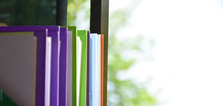 Back view of various plastic file folders for storing important documents in a file box for neatness and easy finding places near glass window, blurred edited background.の写真素材