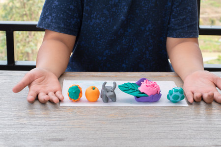 Close up of child hand holding colorful plasticine on wooden table.