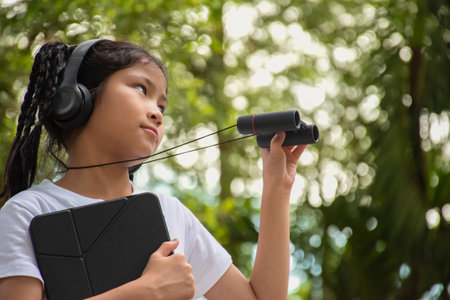 Young asian woman using binoculars and listening to music in the parkの写真素材