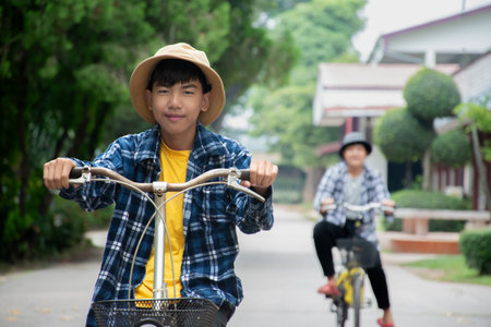 Asian boy riding a bicycle in the park with his father on the backgroundの写真素材