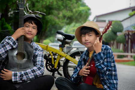 Two asian boys playing guitar by the road in the park.の写真素材