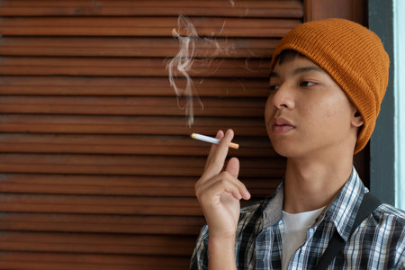 Young asian man in a hat smoking a cigarette on a wooden backgroundの写真素材