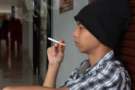 Young Asian man smoking a cigarette in the living room at home.の写真素材