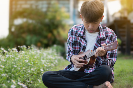 Asian boy playing ukulele in the garden. selective focus.の写真素材
