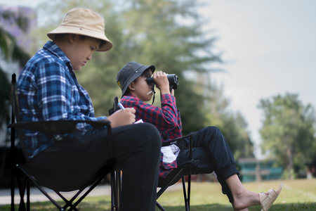 Asian schoolboys spending free times by watching birds, insects, bugs and animals which flying, crawling and climbing on tree branches in tropical forest.の写真素材