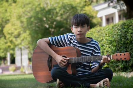 Asian boy playing guitar in the garden, vintage tone and soft focusの写真素材
