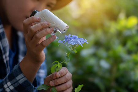 Asian cute schoolboy holds mini portable microscope and looking at the small details of the potted plant in his hand to study and find answer through the lens.の写真素材