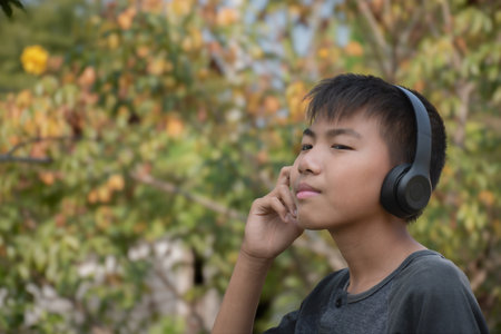 Asian boy using wireless earphones when he listening to music during his long holiday vacation at local park, soft focus, happiness of people in all ages concept, new edited.の写真素材