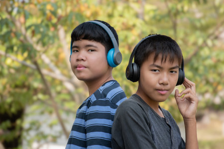 Asian boys using wireless earphones when they listening to music during their long holiday vacation at local park, soft focus, happiness of people in all ages concept, new edited.の写真素材