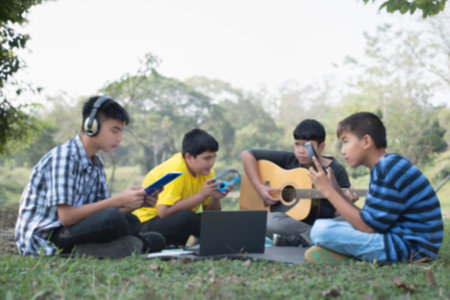 Group of students playing guitar and using laptop computer in the park.の写真素材