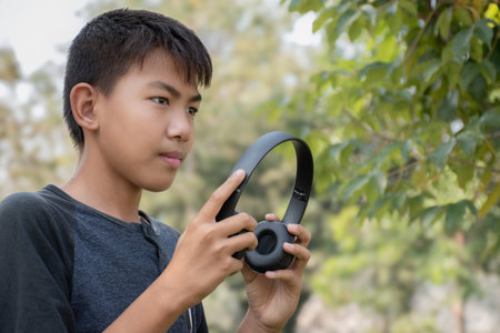 Asian boy using wireless earphones when he listening to music during his long holiday vacation at...