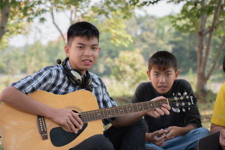Young asian boy playing guitar with his friend in the park.の写真素材