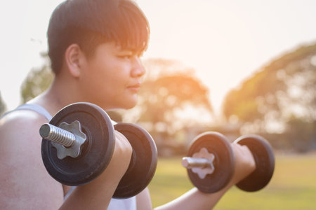 Young asian man lifting dumbbells in the park. Healthy lifestyle concept.の写真素材