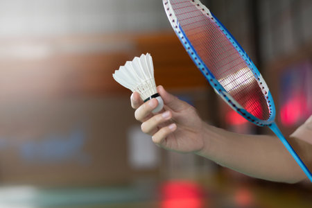 Badminton player holds racket and white cream shuttlecock in front of the net before serving it to another side of the court.の写真素材
