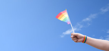 Hand holding lgbt flag on blue sky background with copy space