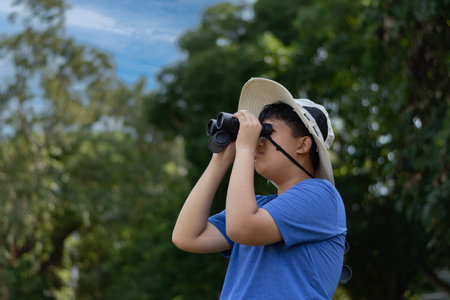 Asian boy exploring nature by using binoculars, Outdoor learning, curiosity, and childhood adventure...