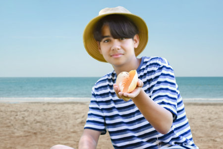 Cute asian boy eating a seashell on the beach.