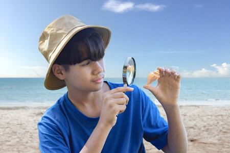 Asian boy looking at seashell through magnifying glass on the beach