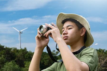 Young man taking photo of wind turbine in the park, Thailand.