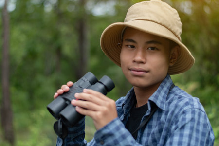 Young asian man wearing hat and holding binoculars in the forestの写真素材