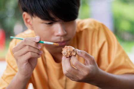 Young asian boy painting a seashell in the park.の写真素材