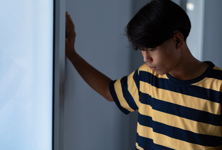 Asian boy in yellow striped t-shirt looking through the window.